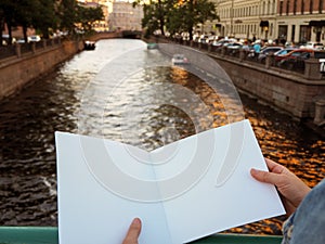 Mockup of blank notebook in female hands on the city river background.