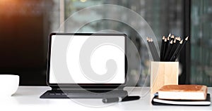 Mockup blank screen tablet with magic keyboard on wooden table in office.