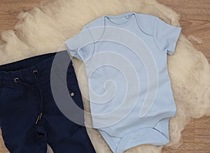 Mockup of blue baby bodysuit on wood background with jeans. Blank baby clothes template mock up. Flat lay styled stock photo