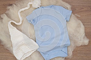 Mockup of blue baby bodysuit on wood background with knitted hat. Blank baby clothes template mock up. Flat lay styled stock photo