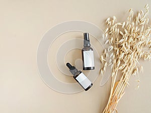 Two amber bottles with white labels and bouquet of dry oats on beige background