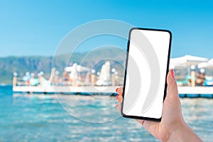 Mockup cell phone image. hand holding white mobile phone with sea and beach blue sky background. roaming on vacation