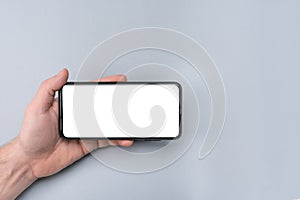 Mockup cell phone. male hand holding phone horizontally with blank white screen. grey table background. copy space Mockup phone photo