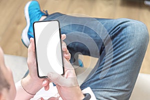 Mockup cellphone. Man sitting on a sofa and holding a blank screen mobile phone