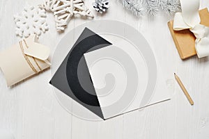Mockup Christmas black greeting card letter in envelope and gift, flatlay on a white wooden background, with place for