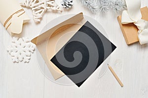 Mockup Christmas black greeting card letter in envelope and pencil, flatlay on a white wooden background, with place for