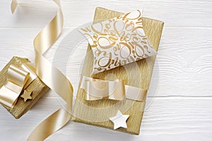 Mockup Christmas greeting card text Hohoho with gold gift ribbon, flatlay on a white wooden background
