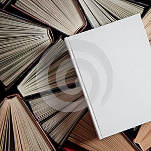 Mockup of closed blank square book rests on open old multicolored books