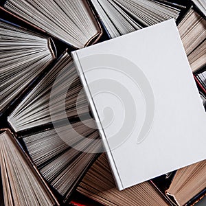 Mockup of closed blank square book rests on open old multicolored books