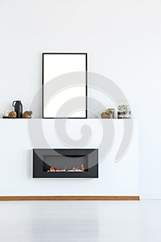 Mockup of empty poster above black fireplace in simple white living room interior. Real photo
