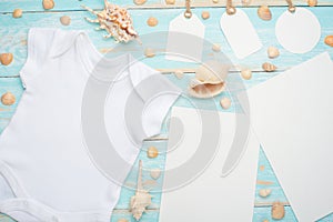 Mockup Flat Lay white baby shirt bodysuit mock-up paper and tags for design on a blue wooden background with a nautical theme,