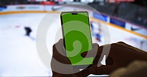 Mockup Green Screen Smartphone. Close Up. Chroma Key Image Of man`s Hands Holding Mobile Phone. Against the Background of the TV a