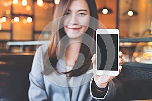 Asian beautiful business woman holding and showing white mobile phone with blank black screen and smiley face in cafe