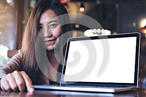 Mockup image of an Asian business woman presenting and showing laptop with blank white screen on wooden table