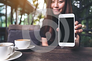 Mockup image of a beautiful woman holding and showing white mobile phone with blank black screen with coffee cups