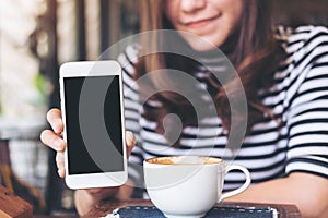 Mockup image of a beautiful woman holding and showing white mobile phone with blank black screen with smiley face and coffee cup o