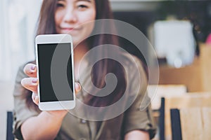 A beautiful woman holding and showing white mobile phone with blank black screen with smiley face in vintage wooden cafe