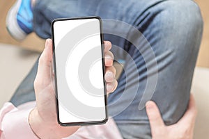 Mockup image blank white screen cell phone. Man hand holding texting using mobile on sofa at home. Empty space for advertise text