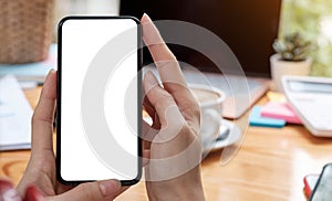 Mockup image blank white screen cell phone.women hand holding texting using mobile on desk at home office