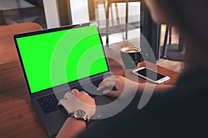 Mockup image of business woman using and typing on laptop with blank green screen , coffee cup and mobile phone on wooden table