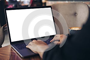 Mockup image of business woman using and typing on laptop with blank white desktop screen and coffee cup on wooden table