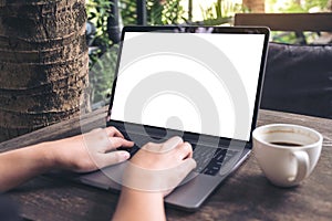 Mockup image of business woman using and typing on laptop with blank white screen and coffee cup on wooden table