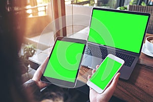 Mockup image of a businesswoman holding white mobile phone , black tablet and laptop with blank green screen on vintage wooden tab