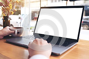 Mockup image of a businesswoman`s hand using laptop with blank white desktop screen while drinking hot coffee on wooden table