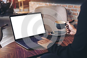 Mockup image of a businesswoman using laptop with blank white desktop screen while drinking hot coffee on wooden table