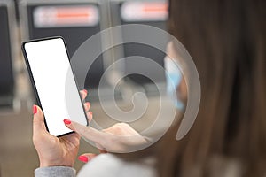 Mockup image of female hands holding black mobile phone with blank white screen over flight board in airport terminal. Woman Using