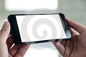 A hand holding black mobile phone with blank white desktop screen in cafe