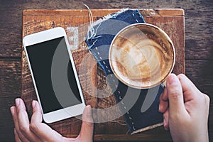 Mockup image of a hand holding mobile phone with blank black screen and coffee cup