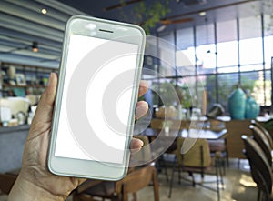 Mockup image of hand holding mobile phone at blur coffee shop background with blank white screen