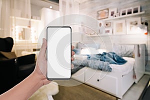 Mockup image of  hand holding modern mobile phone with blank copy space desktop screen for your advertisement in bedroom