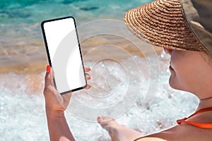 Mockup image of a hand holding and showing modren mobile smart phone in front of the beach in summer with blue sea background. Sea