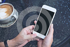 Mockup image of a hand holding white mobile phone with blank black screen and coffee cup