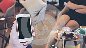 Mockup image of a hand holding white mobile phone with blank black screen in modern cafe