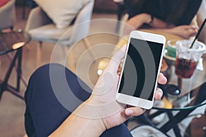 Mockup image of a hand holding white mobile phone with blank black screen in modern cafe