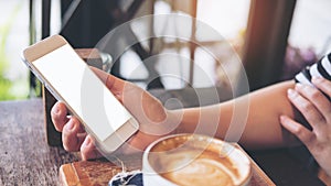 Mockup image of hand holding white mobile phone with blank screen with coffee cup on wooden table