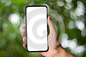 Mockup image of hand holding white mobile phone with blank white green nature background