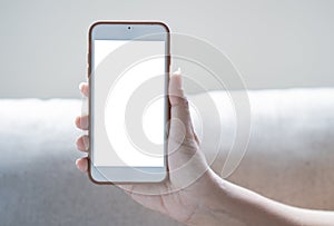 Mockup image of hand holding white mobile phone with blank white screen on light beige sofa background