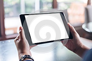 Mockup image of hands holding black tablet pc with white blank screen on wooden table background