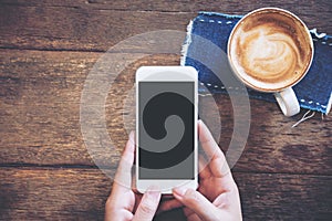 Mockup image of hands holding white mobile phone with blank black screen with coffee cups