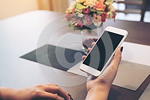 Mockup image of hands holding white smartphone with blank black desktop screen and laptop