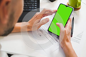 Mockup image, man hand holding blank green screen mobile smart phone, working on laptop