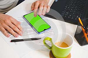 Mockup image, man hand touching blank green screen mobile smart phone, working on laptop