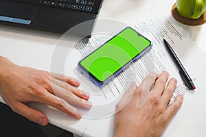 Mockup image, man hands near blank green screen mobile smart phone, working on laptop