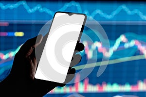 Mockup image of a smartphone with the blank white screen in a hand and stock chart on the background