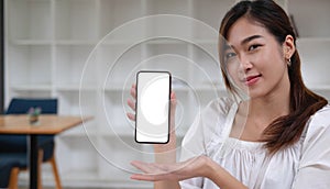 Mockup image of a smiley Asian beautiful woman holding and showing black mobile phone with blank white screen.