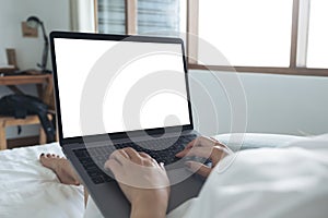 Mockup image of a woman lying on a bed , using and typing on laptop with blank white desktop screen